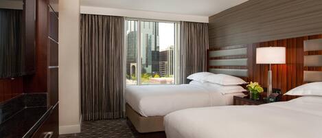 A hotel room with two beds, a large window with curtains, a TV, and a nightstand with a lamp and flowers.