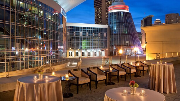 An outdoor dining area with round tables and chairs, set against a backdrop of modern buildings and a clear sky. - Hilton Nashville Downtown (Nashville)