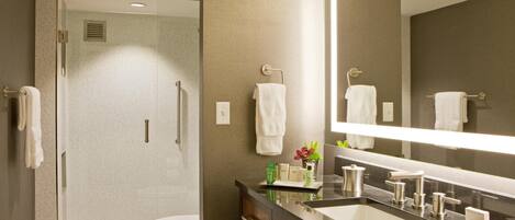 Un baño moderno con ducha envuelta en vidrio, un espejo grande y un mueble de tocador con lavamanos y toallero.
