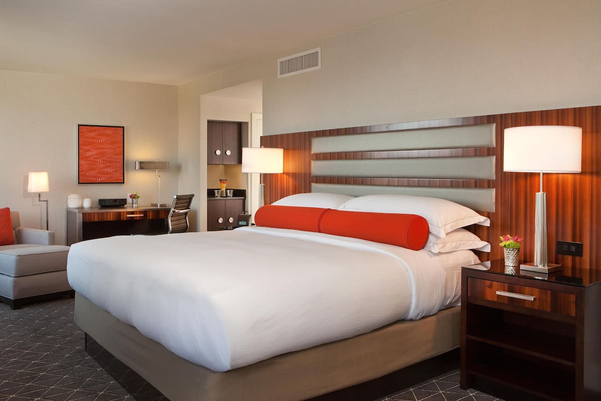 A hotel room with a large bed, a desk, a chair, a nightstand, and a wall-mounted lamp.