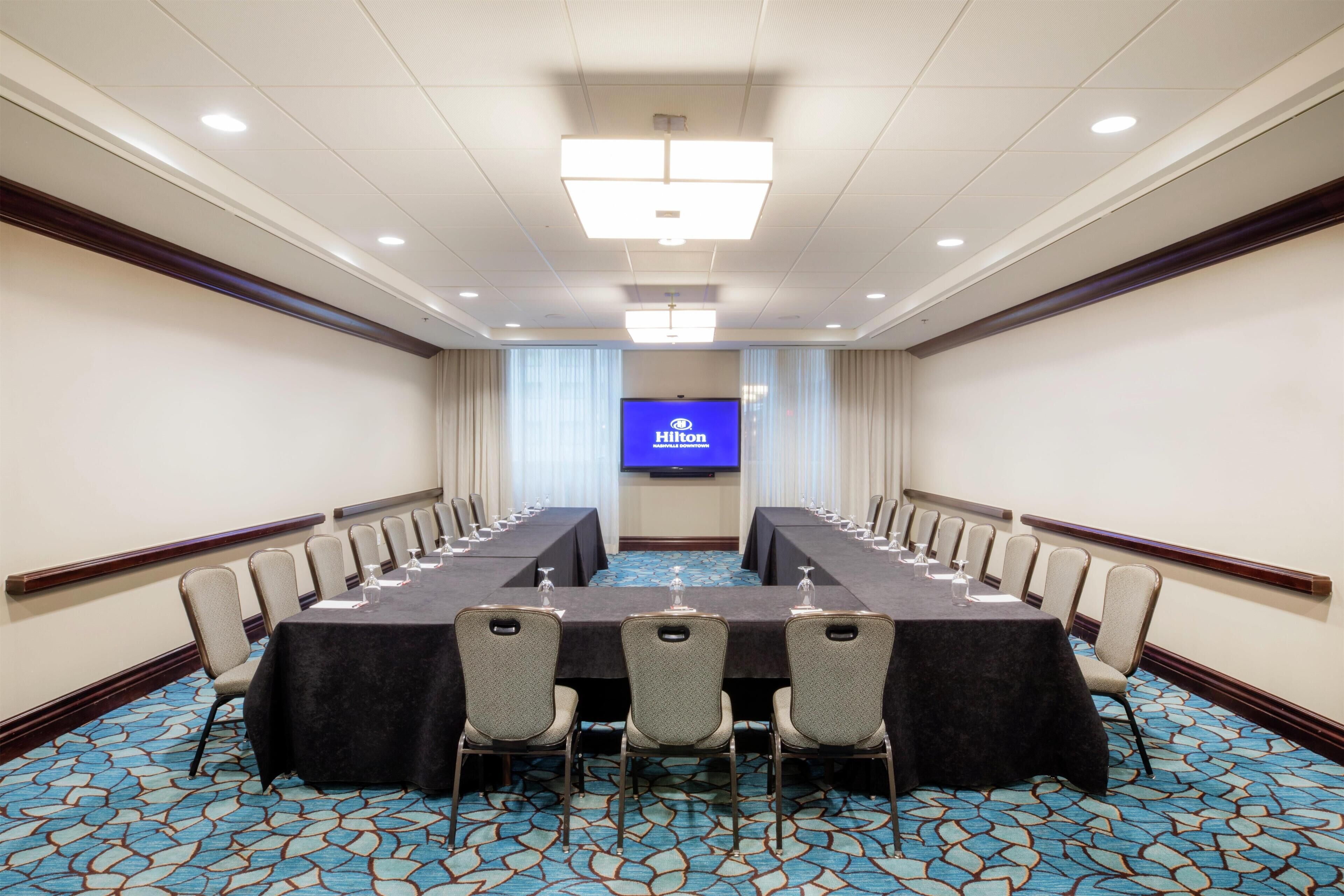Un salón de conferencias con una larga mesa, sillas y una pantalla grande que muestra el logo de Hilton.