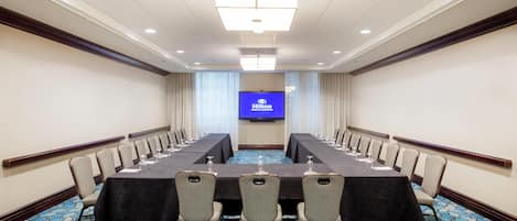 Un salón de conferencias con una larga mesa, sillas y una pantalla grande que muestra el logo de Hilton.