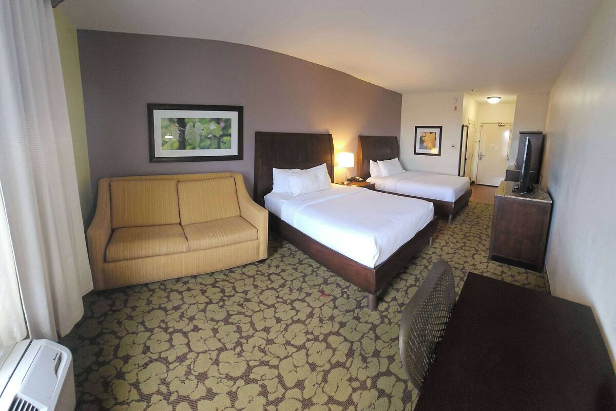 A hotel room with two beds, a sofa, a TV, and a heater.