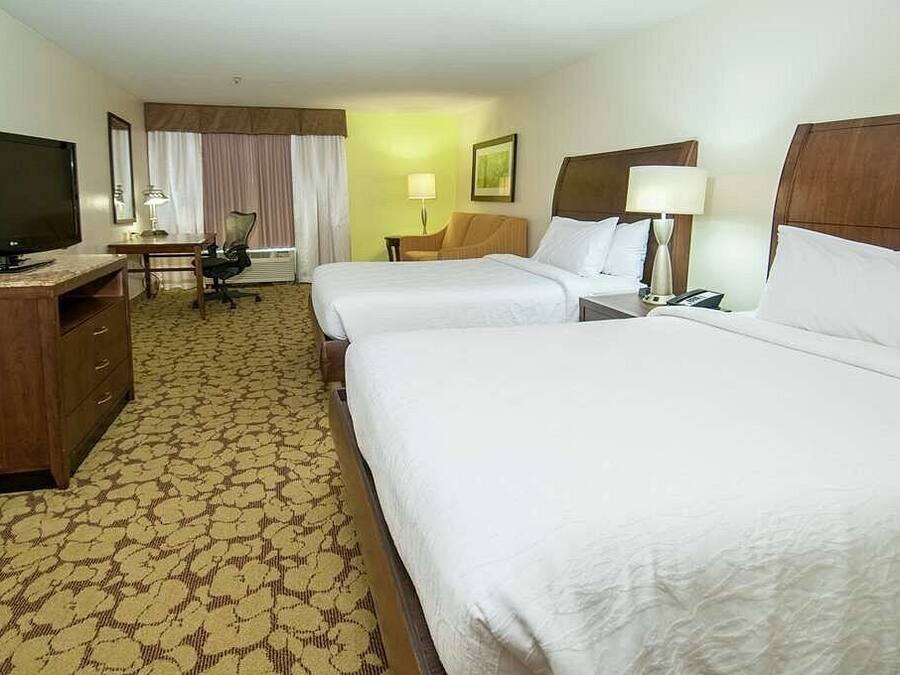 Habitación de hotel con dos camas, un escritorio, televisión, una silla y una lámpara.