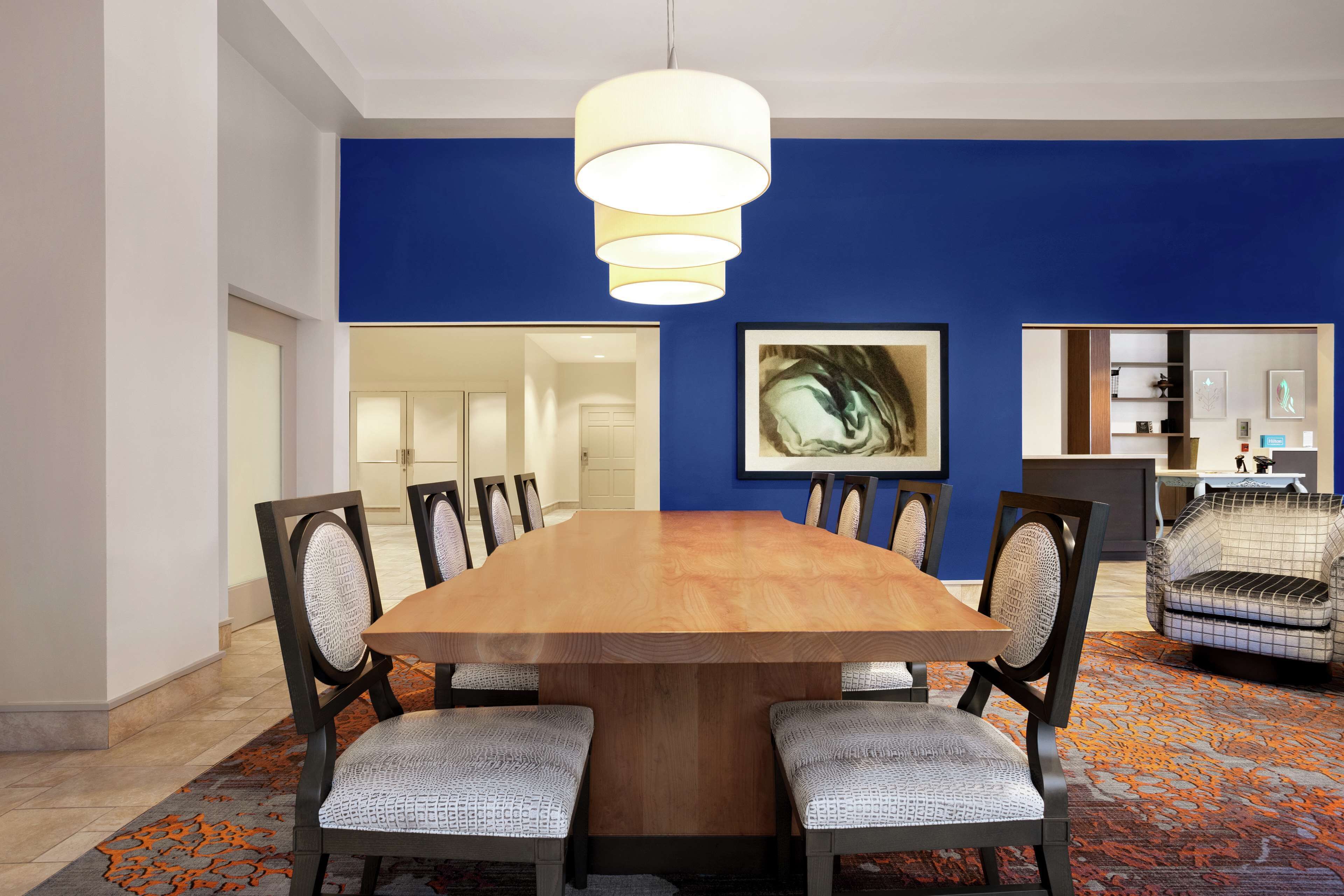 A dining area with a wooden table, six chairs, a blue accent wall, and a large painting.