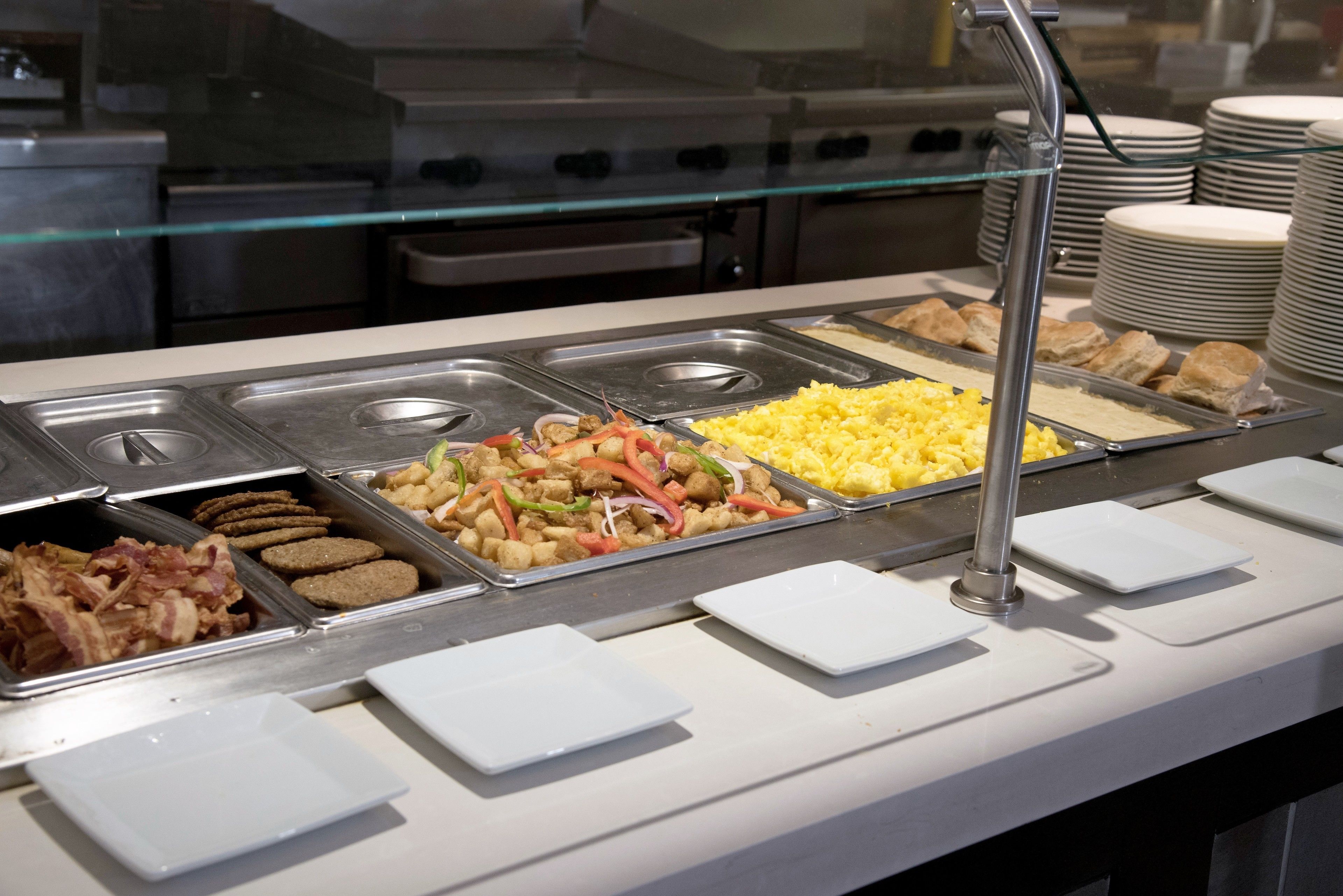 Buffet com diversas opções de comida, incluindo bacon, salsicha, legumes e ovos mexidos.