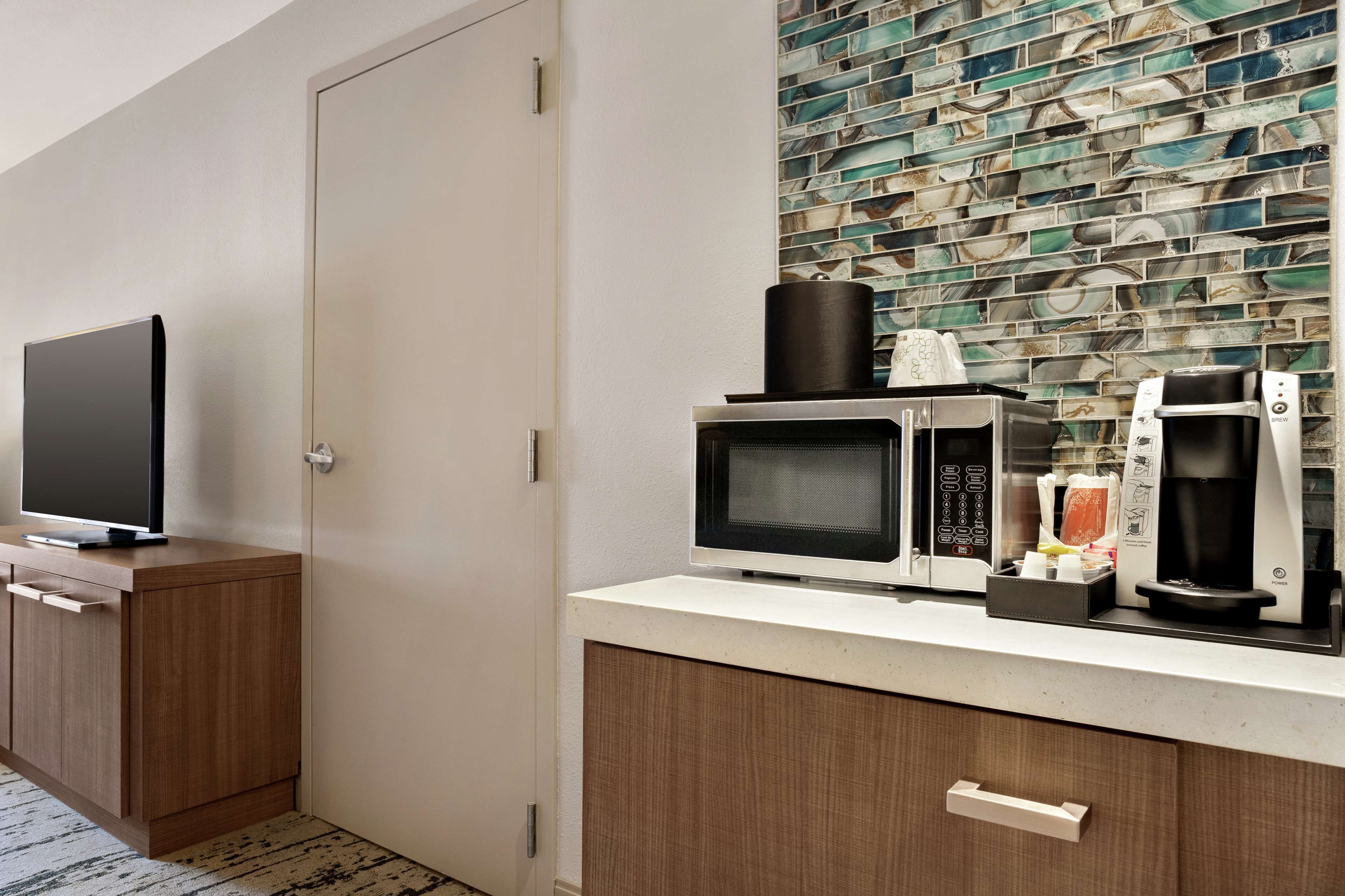 A kitchenette with a microwave, coffee maker, and a flat-screen TV on a wooden cabinet.