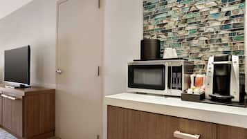 Una kitchenette con microondas, cafetera y un televisor de pantalla plana sobre un mueble de madera.