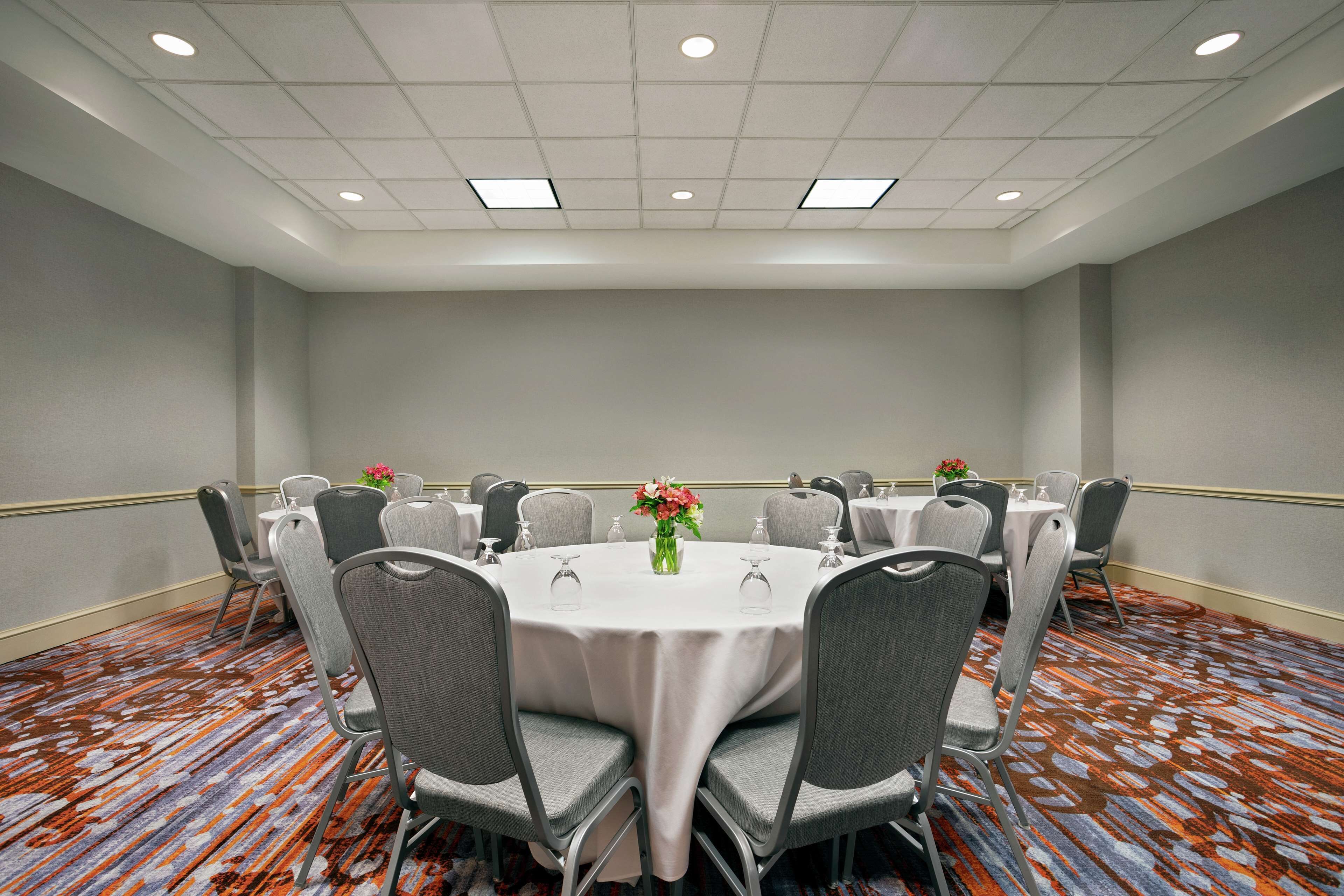 A conference room with a round table, grey chairs, and a floral centerpiece.