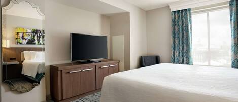 Una habitación de hotel con una cama grande, un televisor de pantalla plana, un aparador de madera, un espejo y una ventana con cortinas.