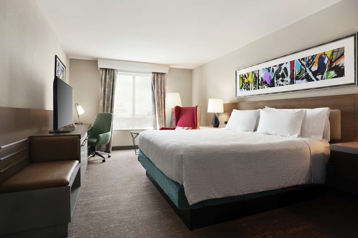 A hotel room with a large bed, a desk with a computer, a chair, and a TV.