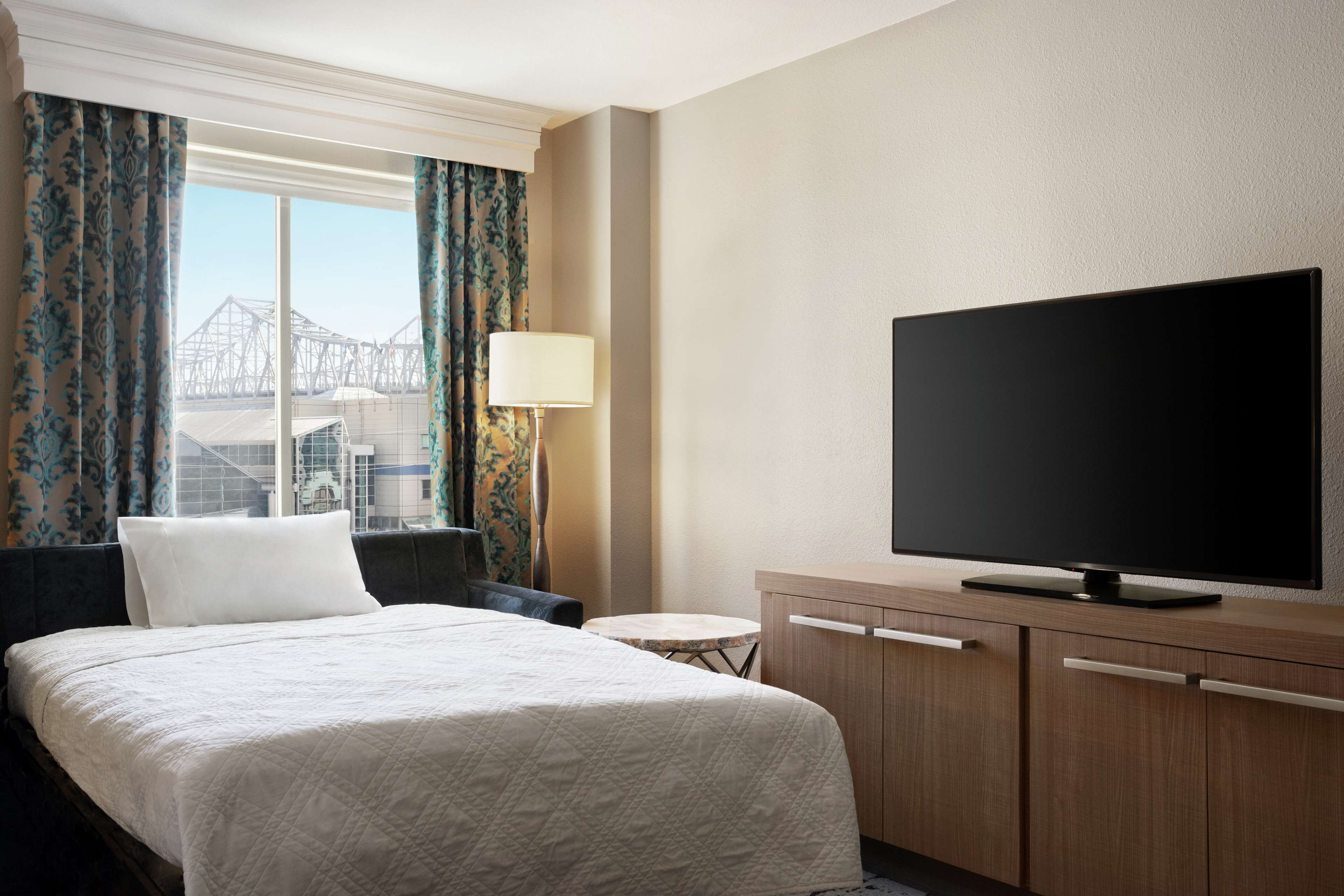 Habitación de hotel con cama, televisor, una mesita y vista a un puente.