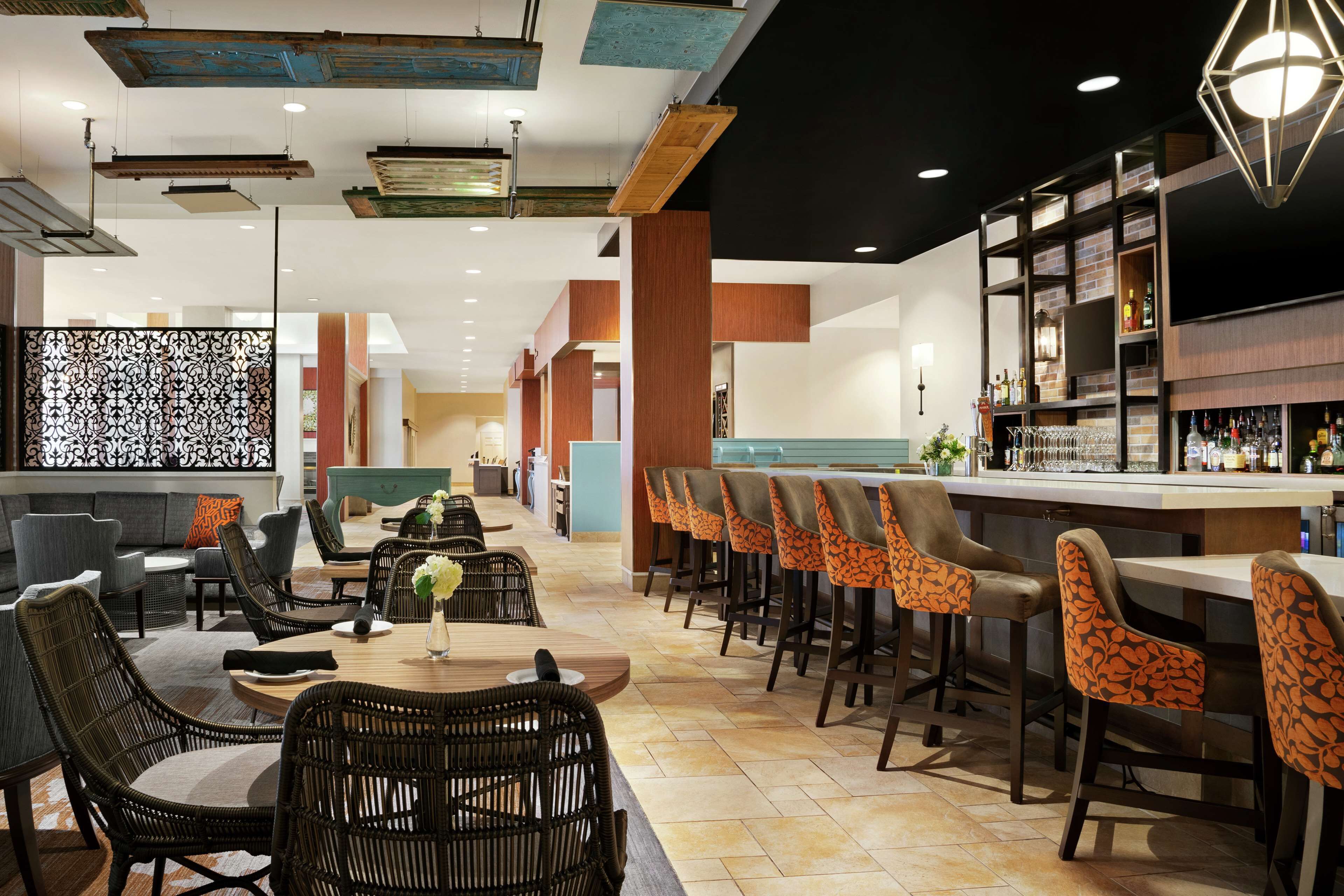 A modern bar area with wicker furniture, a counter with bar stools, and a variety of bottles and glasses.