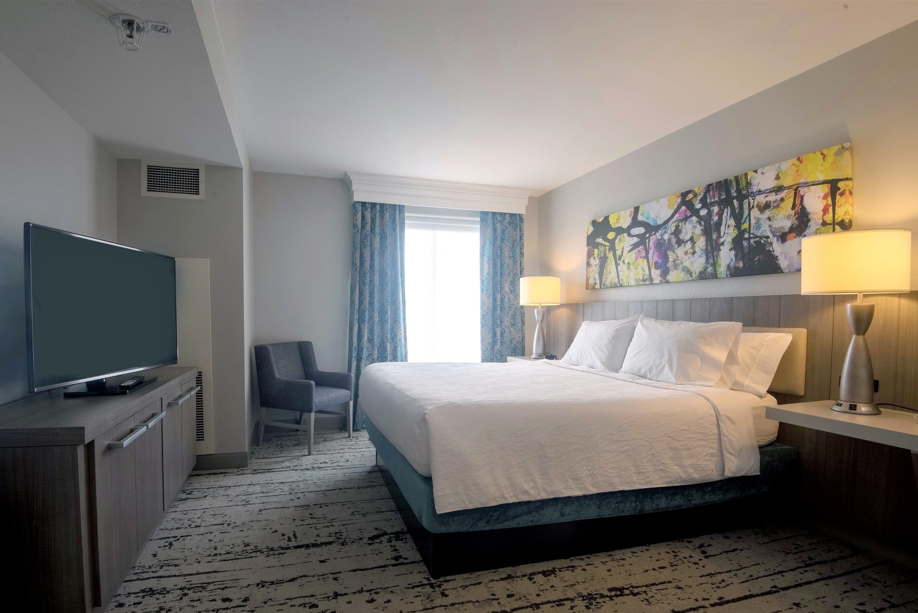 Une chambre d’hôtel avec un lit, une télévision, un bureau et un tableau au mur.
