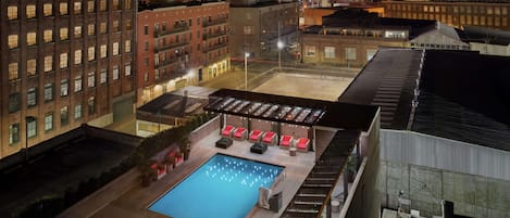 A rooftop pool area with seating and a view of the cityscape at night.