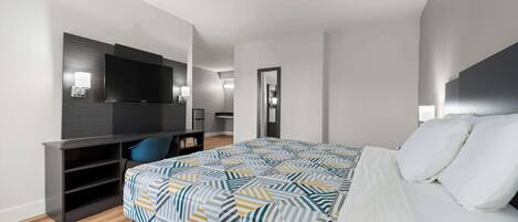 A modern hotel room with a large bed, a desk with a chair, a flat-screen TV, and a mirror.