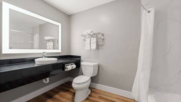 Une salle de bain moderne avec un plan de toilette noir, un lavabo blanc et des toilettes. On y trouve un porte-serviettes au mur et un rideau de douche.