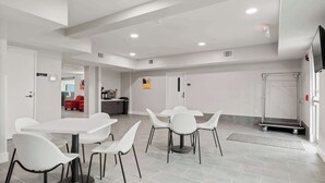 Una habitación de hotel moderna con muebles blancos, una zona de cocina y una silla roja al fondo.