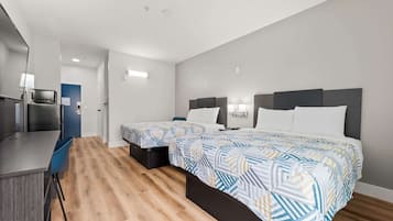 A modern hotel room with two single beds, a small desk, and a kitchenette.