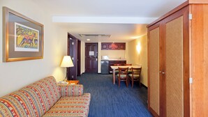 Una habitación de hotel con sofá, una mesa de comedor con sillas, una zona de cocina y un armario.