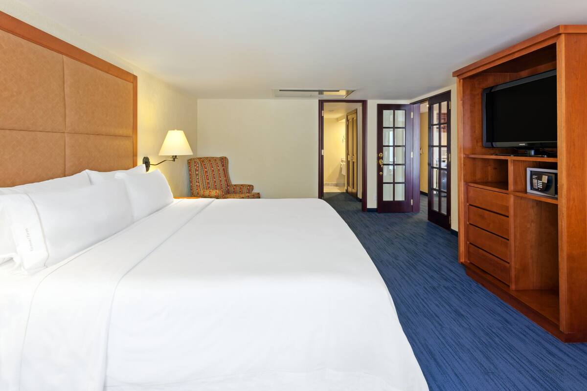 A hotel room with a large bed, a television, a desk, and a chair.