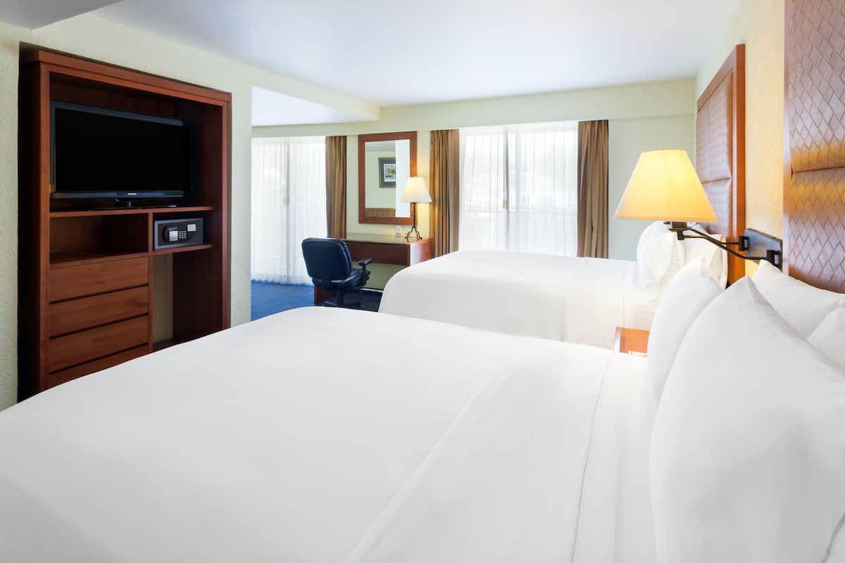 A hotel room with two beds, a desk, a chair, a television, and a lamp.