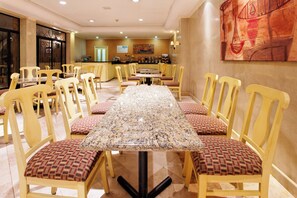 Un comedor de hotel con una mesa larga, varias sillas y una cocina al fondo.