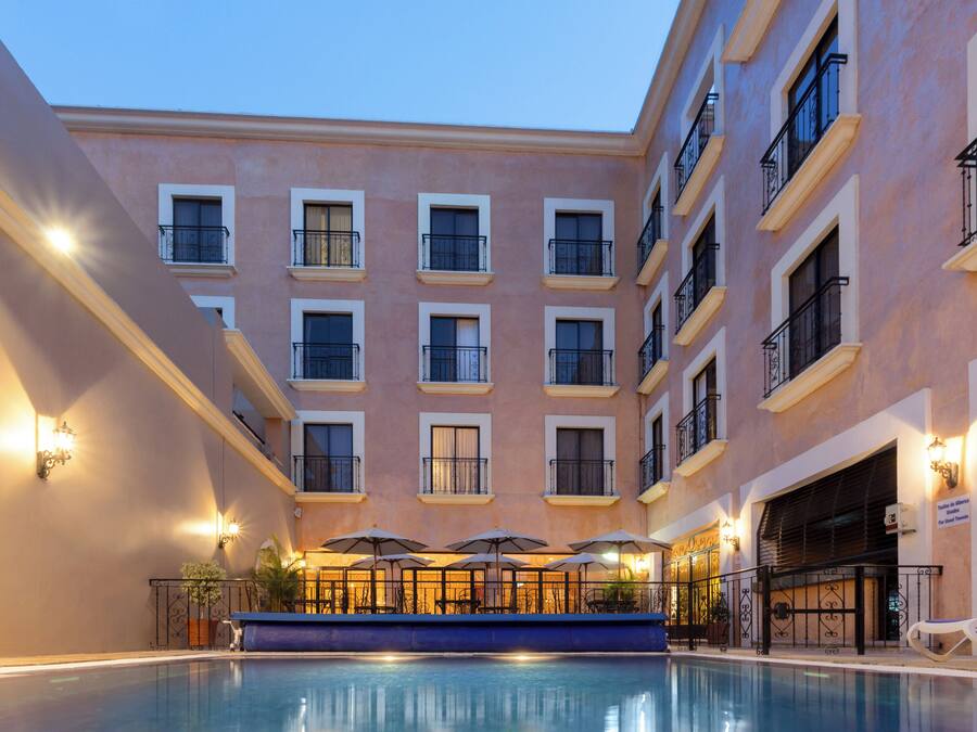 Un hotel con piscina, varios balcones y mobiliario exterior con sombrillas.
