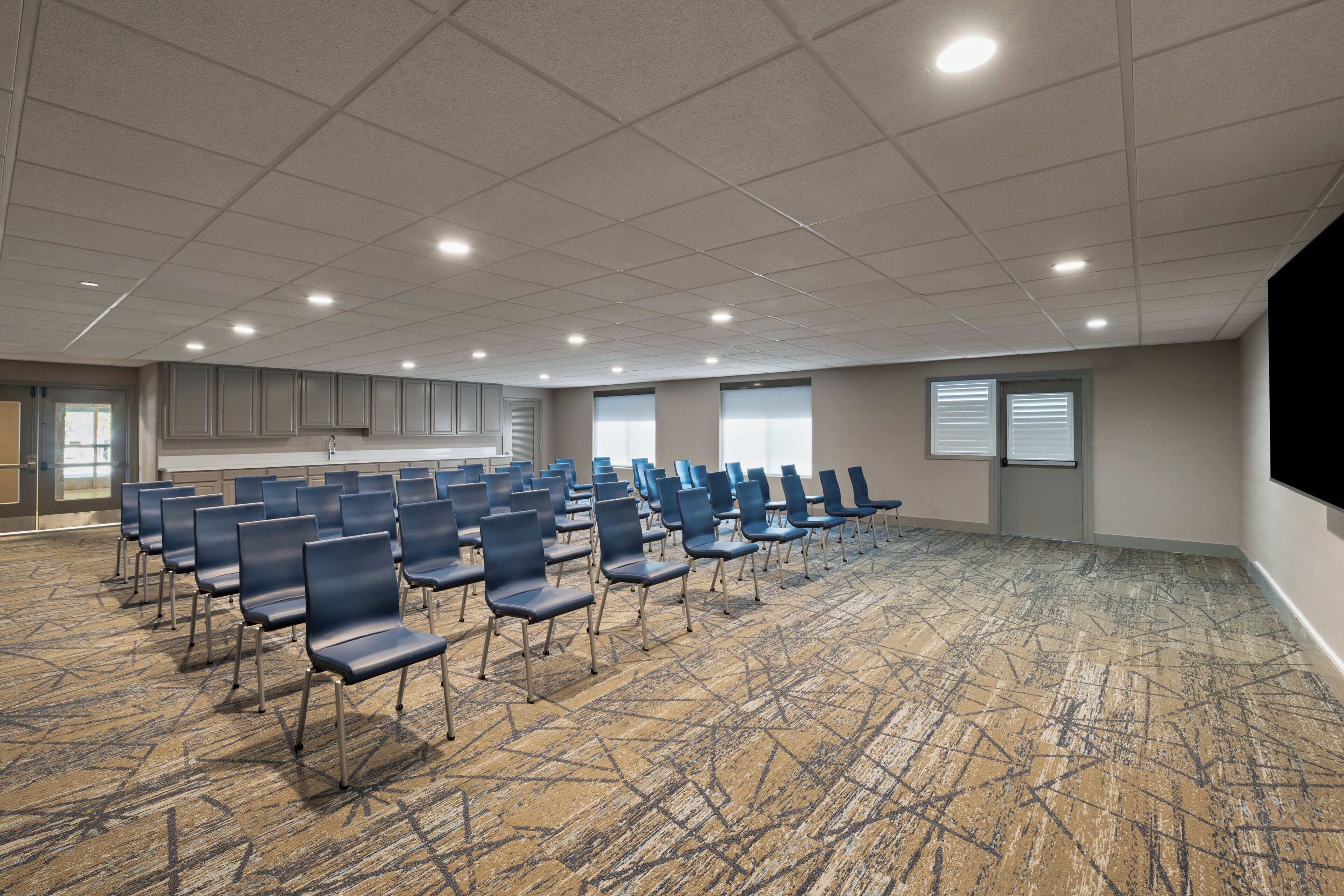 A conference room with rows of chairs, a carpeted floor, and a ceiling with recessed lighting.