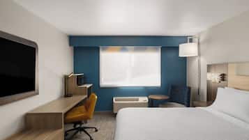 Una habitación de hotel con cama, escritorio, silla, televisor, lámpara y ventana.