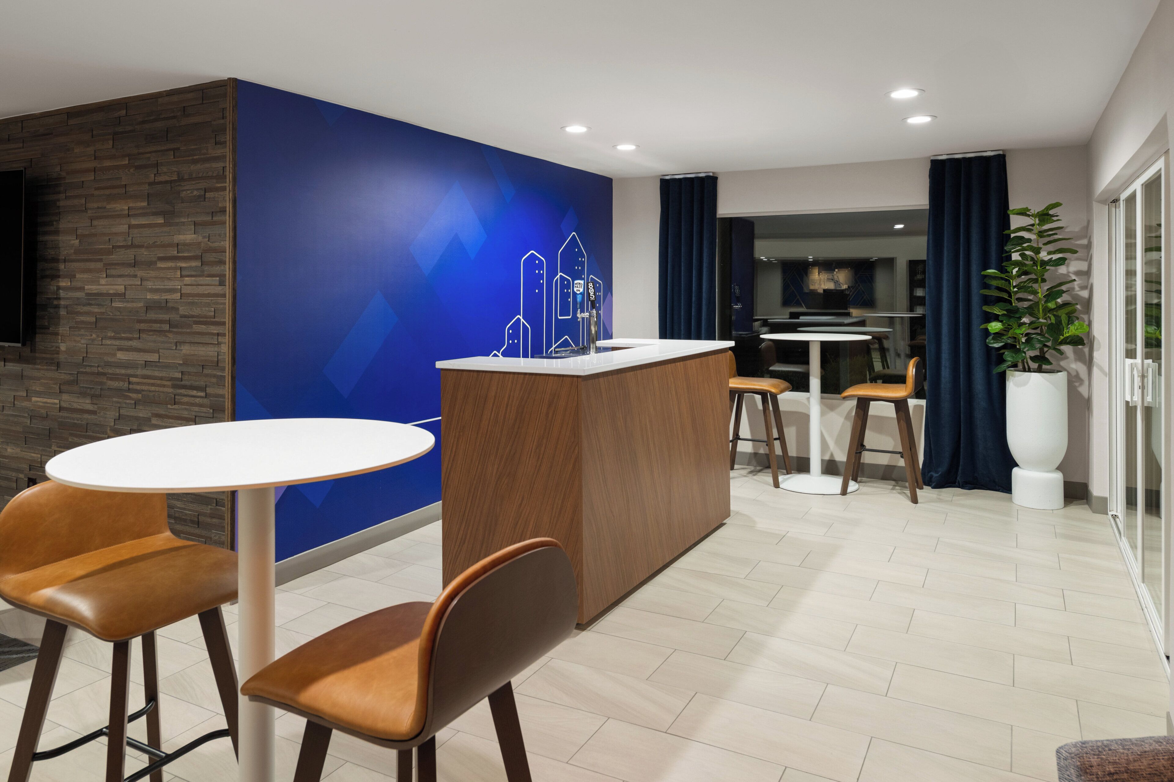 A modern hotel lobby with a bar area, seating, and a large potted plant.