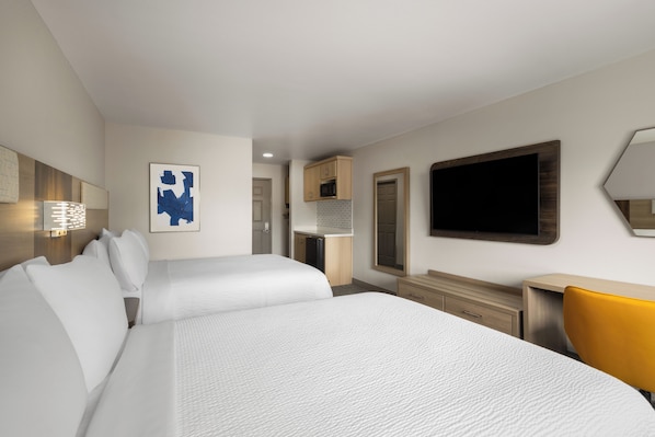Ett hotellrum med två sängar, ett skrivbord, en stol, en tv och ett badrum som syns i bakgrunden.