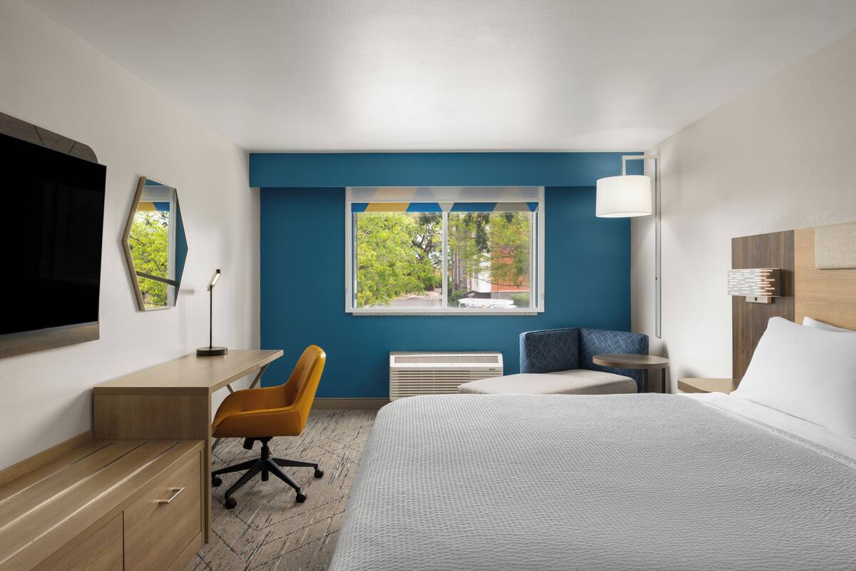 Ein Hotelzimmer mit Bett, Schreibtisch, Stuhl und einem Fenster mit Blick auf Bäume.