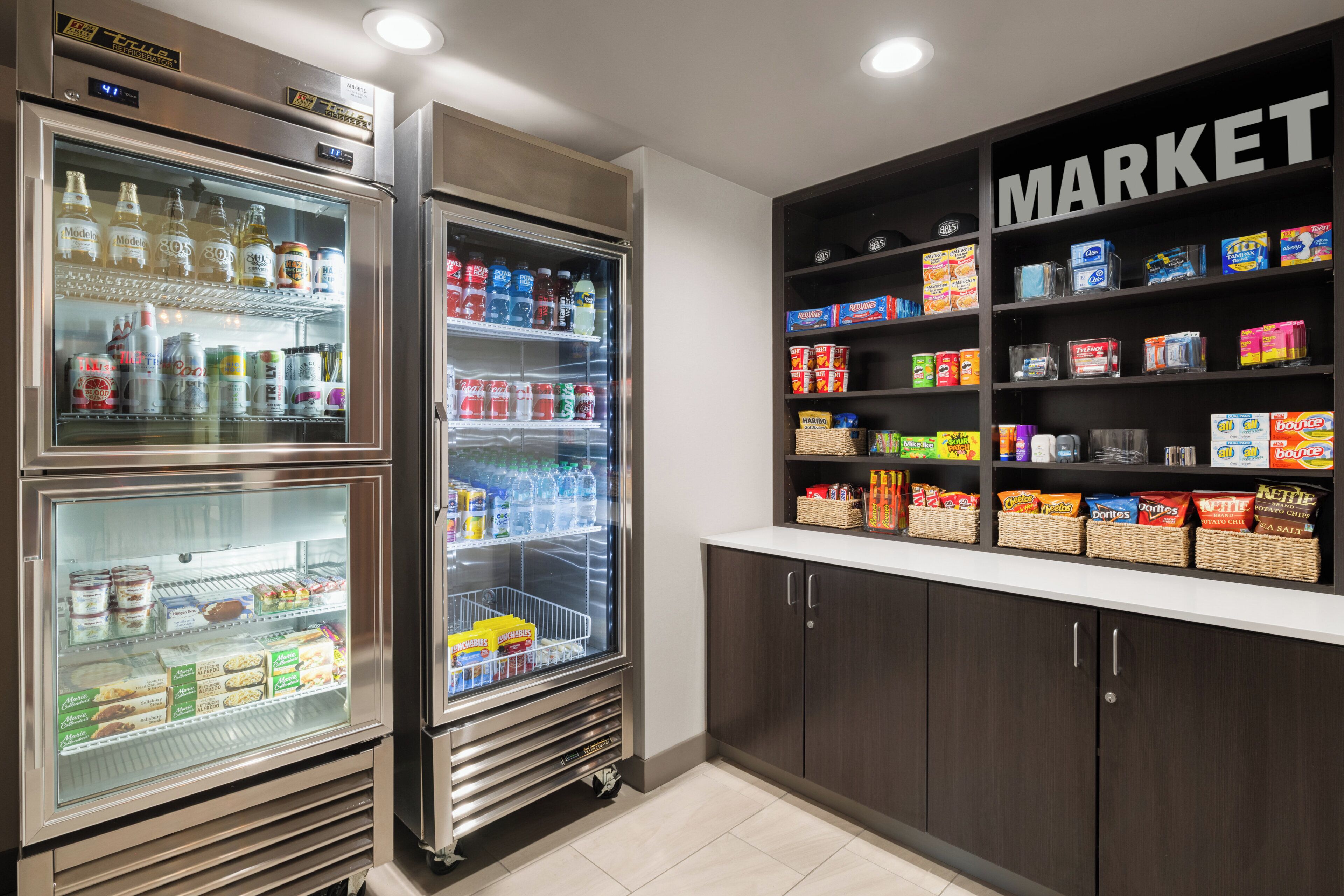A kitchenette with a refrigerator, freezer, and a pantry stocked with snacks and beverages.