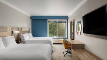 Habitación de hotel con dos camas, un escritorio con silla, un televisor de pantalla plana y un ventanal con vistas a árboles.