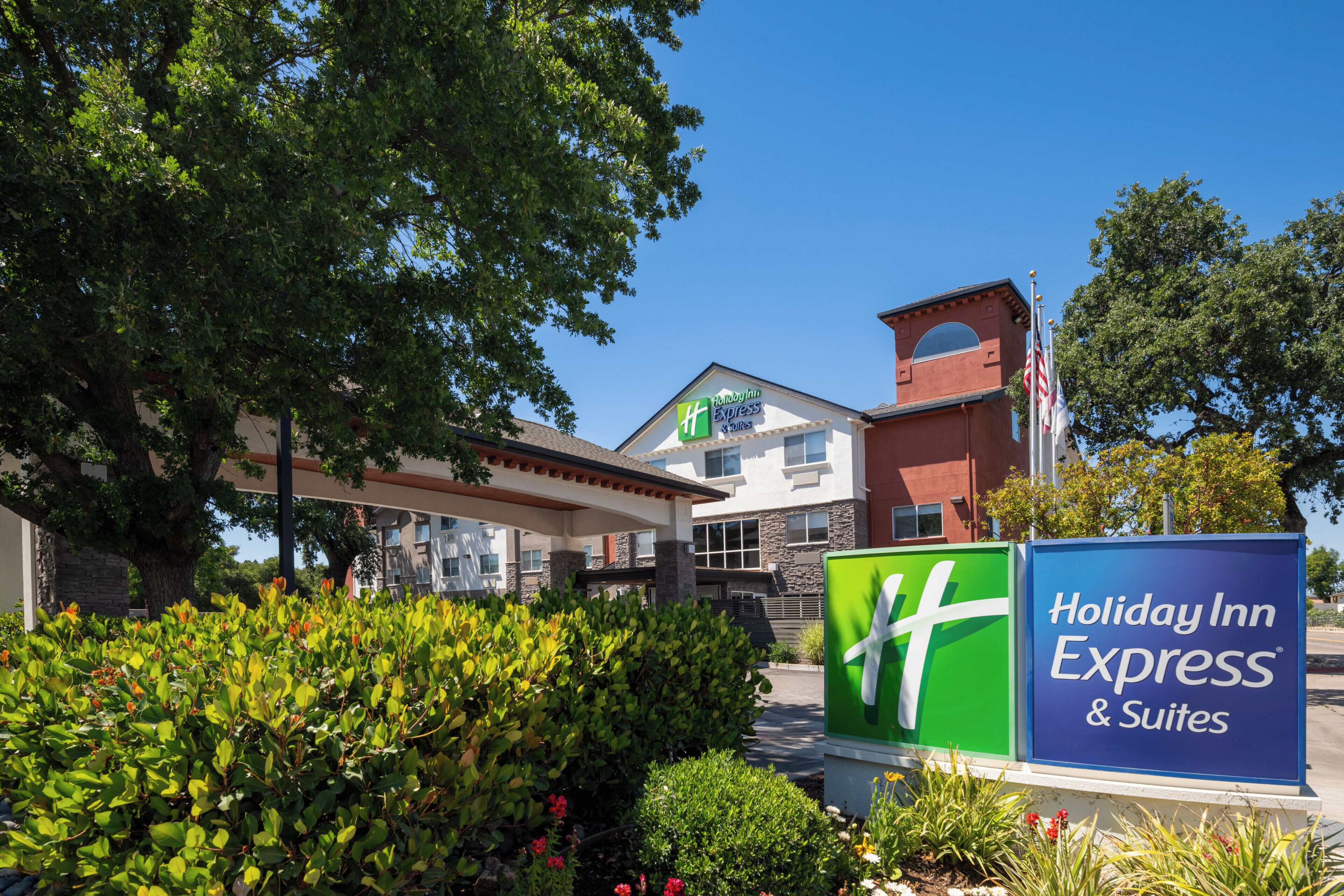 Un Holiday Inn Express & Suites con cielo despejado, rodeado de vegetación y un jardín bien cuidado.