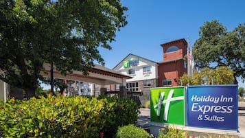 Un Holiday Inn Express & Suites con cielo despejado, rodeado de vegetación y un jardín bien cuidado.