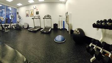 A gym with treadmills, elliptical machines, a stationary bike, a rowing machine, a blue exercise ball, and a rack of dumbbells.