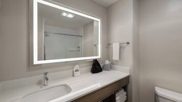 Un baño con un lavamanos blanco, un espejo con luz, un perchero y un inodoro.