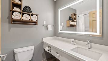 A modern bathroom with a toilet, a large mirror, a sink, and towel storage.