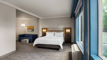 Una habitación de hotel con una cama grande, un sofá, un pequeño taburete y una ventana con cortinas.