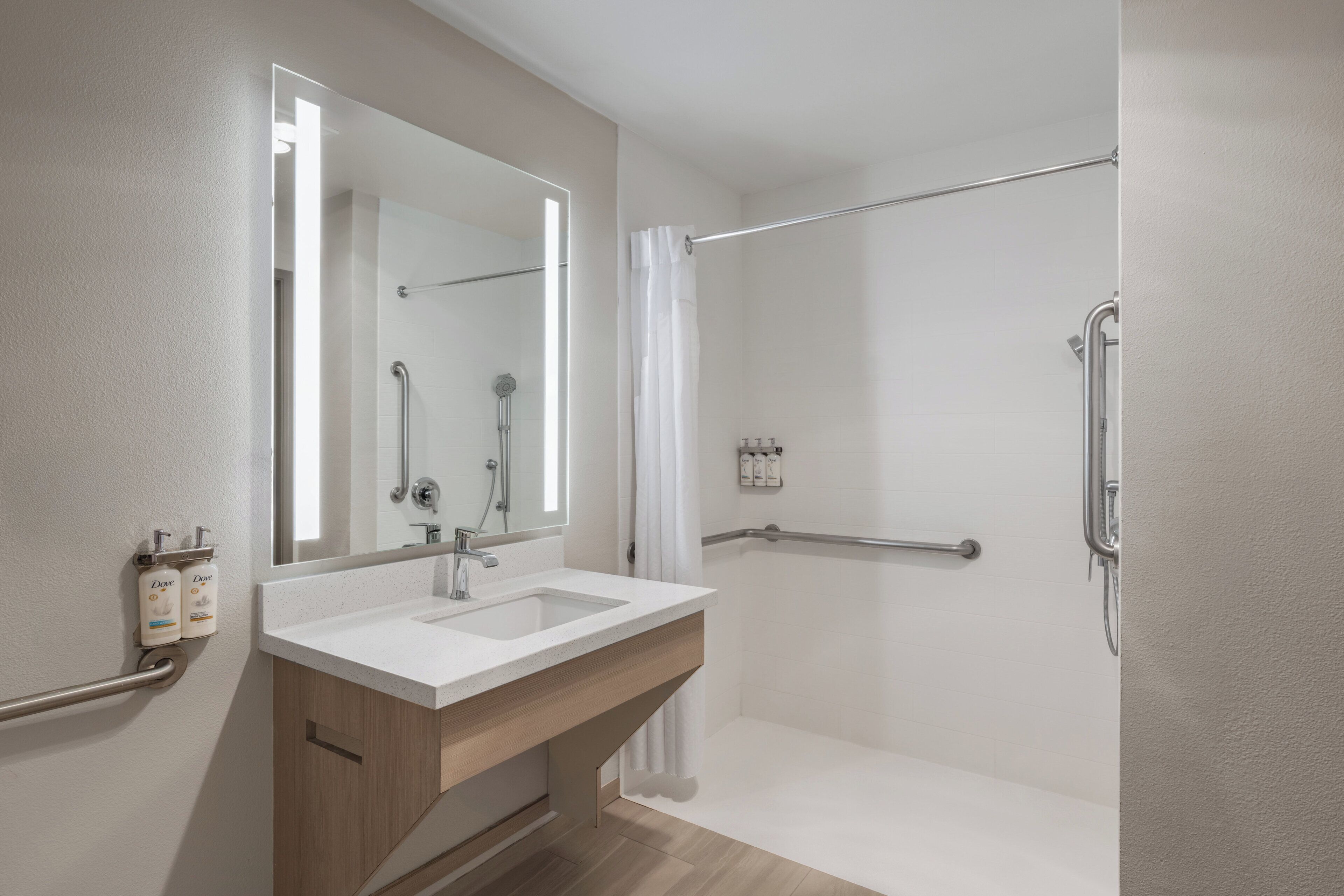 Une salle de bain moderne avec un double lavabo, une douche équipée de barres d’appui et un grand miroir.