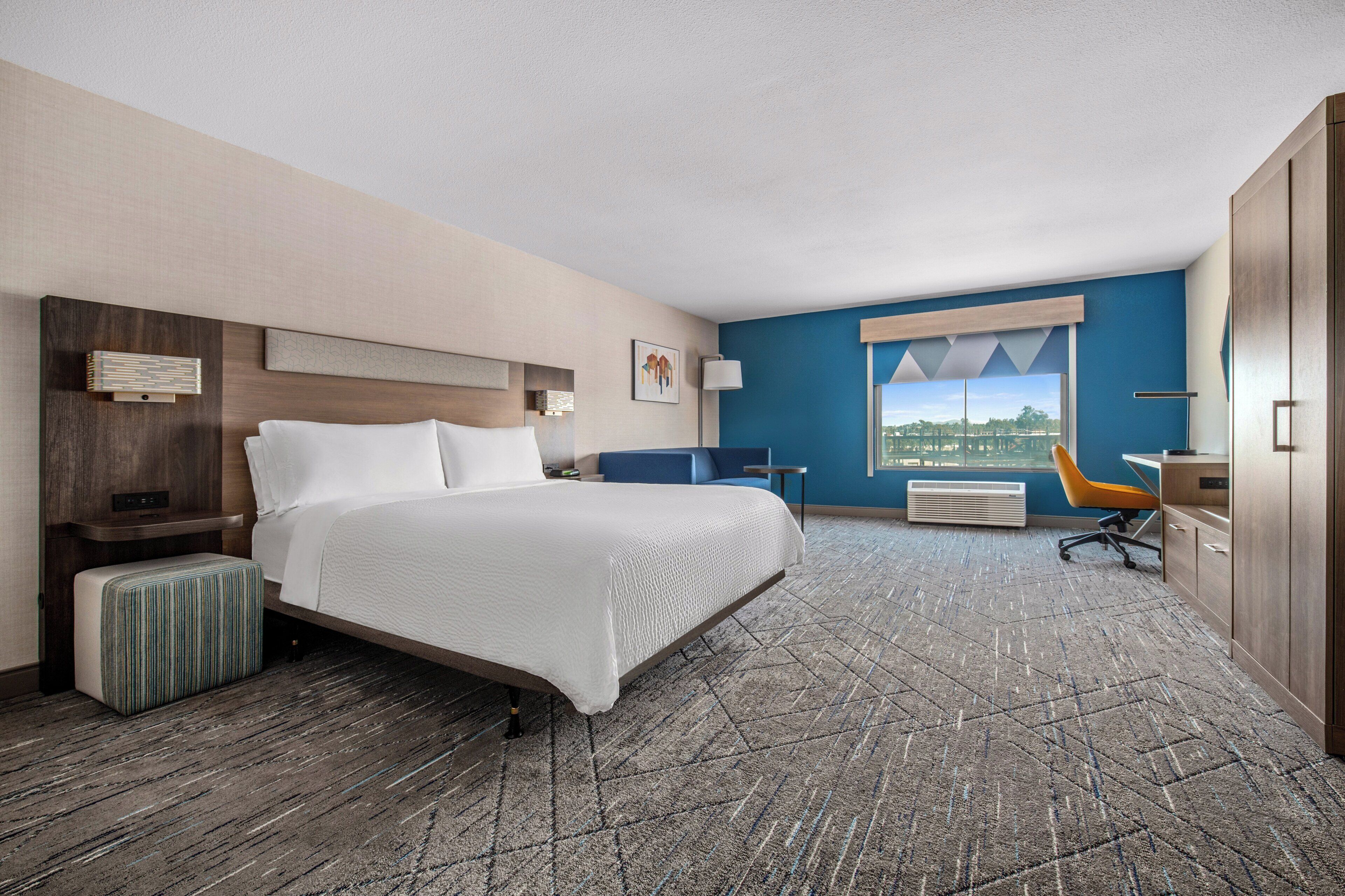 A hotel room with a large bed, a desk, a chair, and a view of the city.