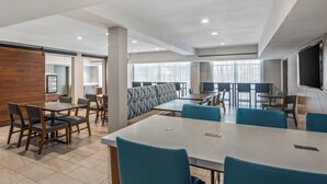 Un espace de restauration moderne dans un hôtel, avec une longue table commune, des tables individuelles et des chaises bleues.