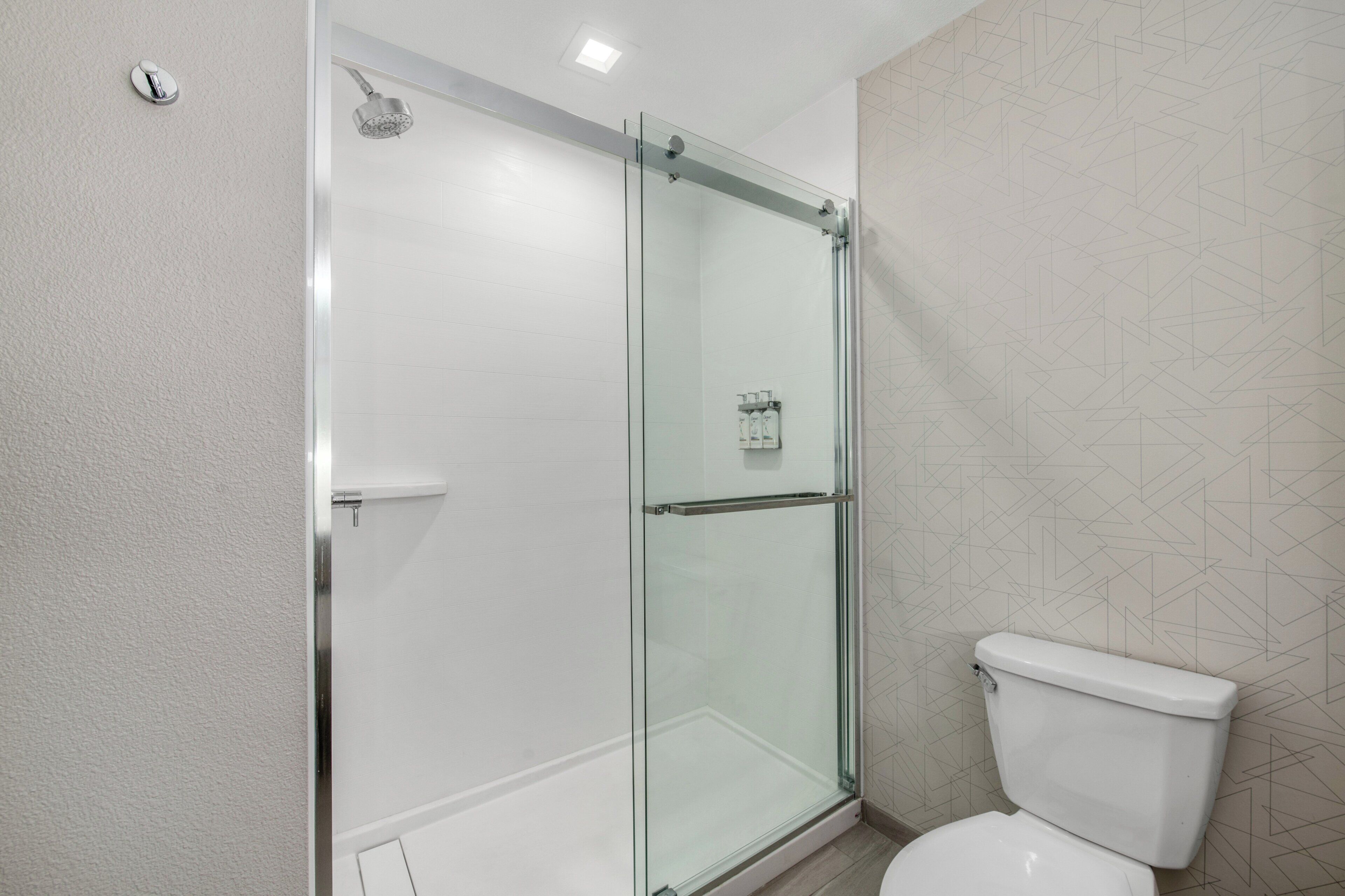 Un baño moderno con ducha de vidrio, inodoro y pared con diseño.