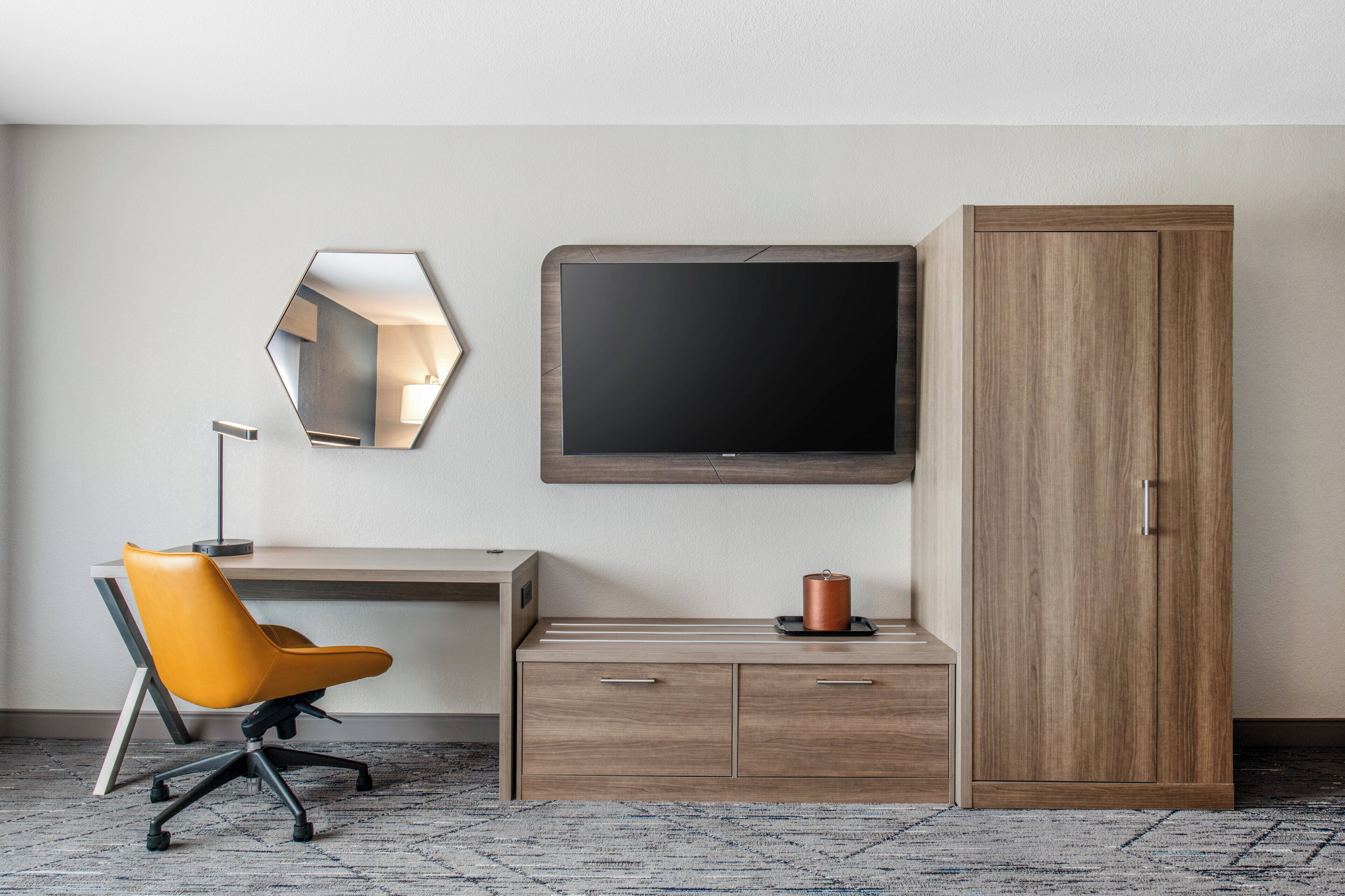 Ein Hotelzimmer mit Schreibtisch, Stuhl, Kleiderschrank, Fernseher und Spiegel.