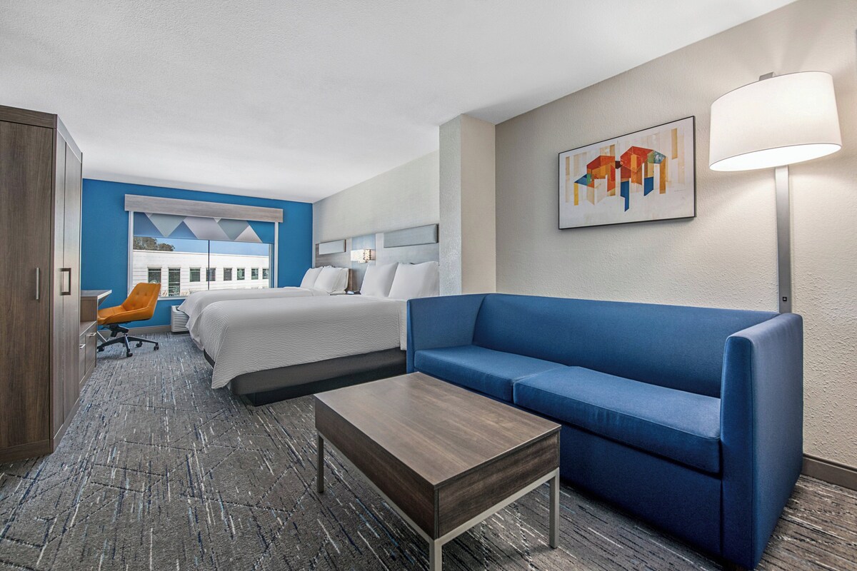 A hotel room with a bed, a blue sofa, a wooden coffee table, and a desk with a chair.
