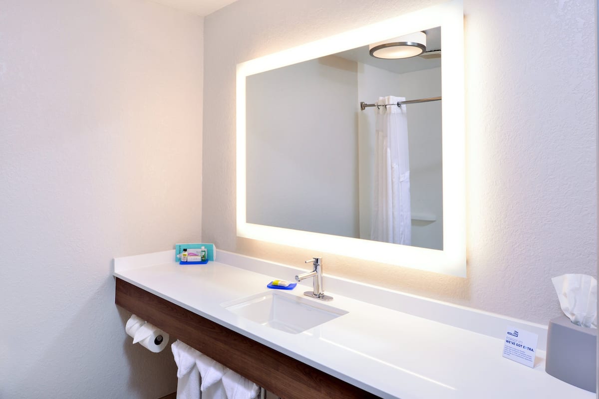A modern bathroom with a white sink, a mirror with built-in lighting, and a towel rack.