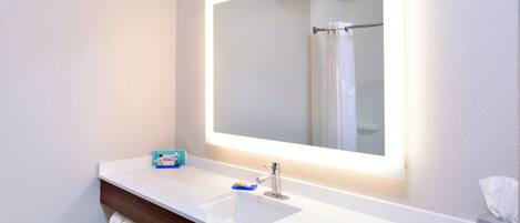 A modern bathroom with a white sink, a mirror with built-in lighting, and a towel rack.
