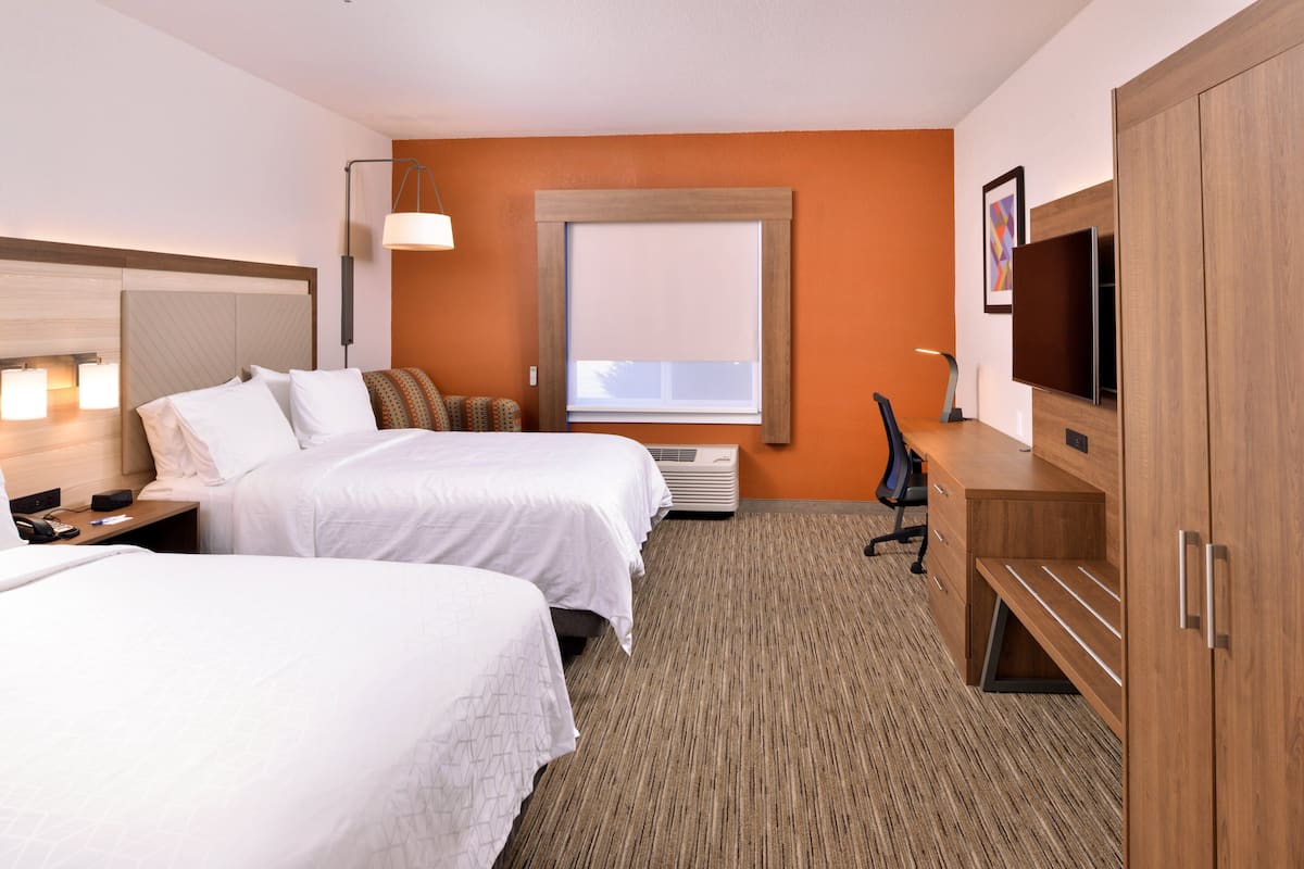 A hotel room with two beds, a desk, a chair, a TV, and a window with blinds.